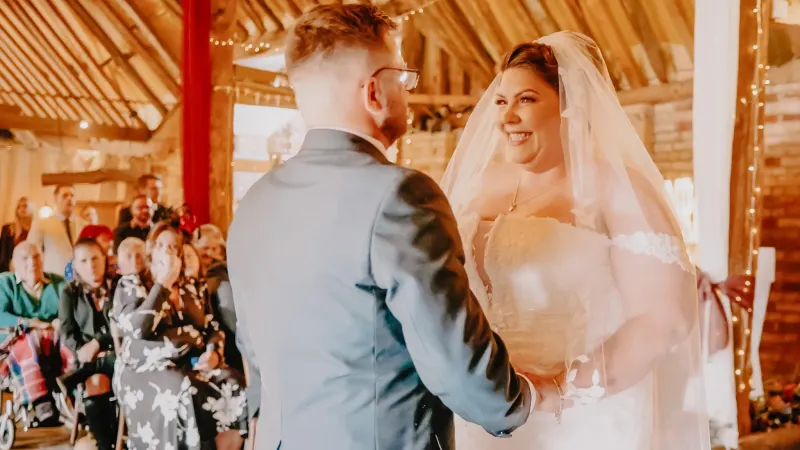 Bride and groom holding hands during their ceremony in a timber barn.